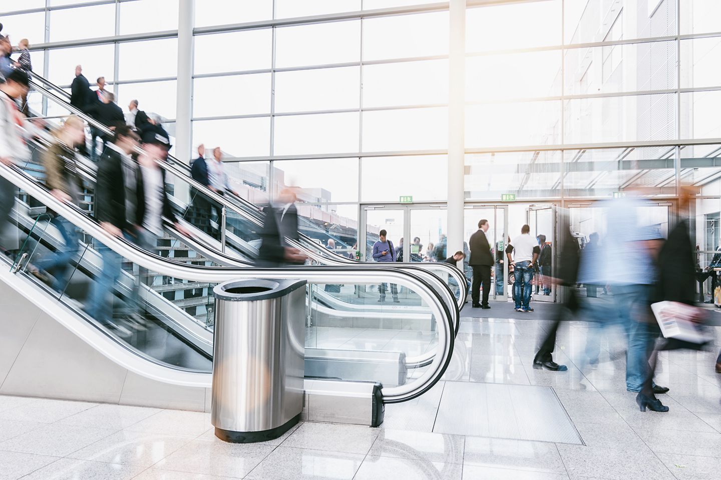 Lower end of an escalator with people walking by in a large glass building