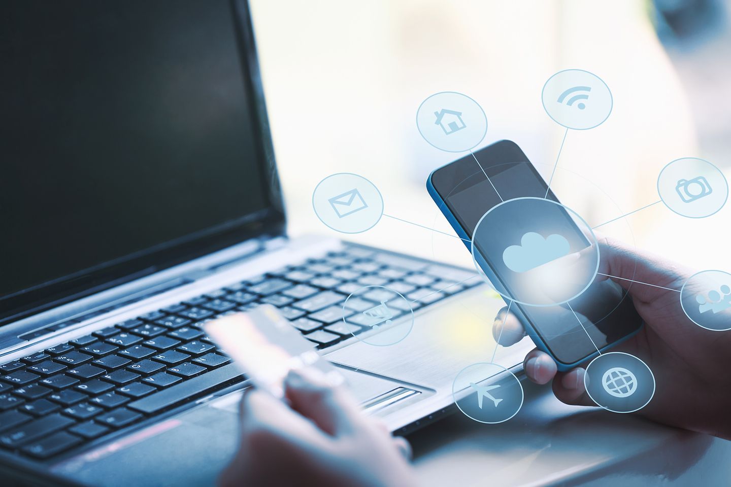 Hands in front of laptop holding card and smartphone, a cloud hologram appears in front of it.