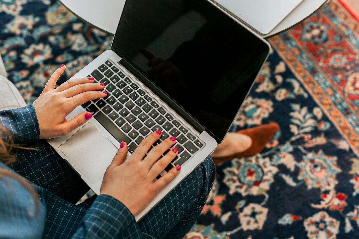 Eine Frau sitzt auf dem Teppich und arbeitet am Laptop