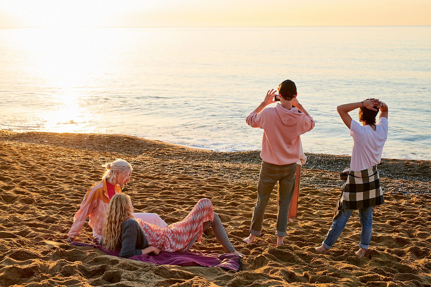 Junge Menschen sitzen und stehen am Strand