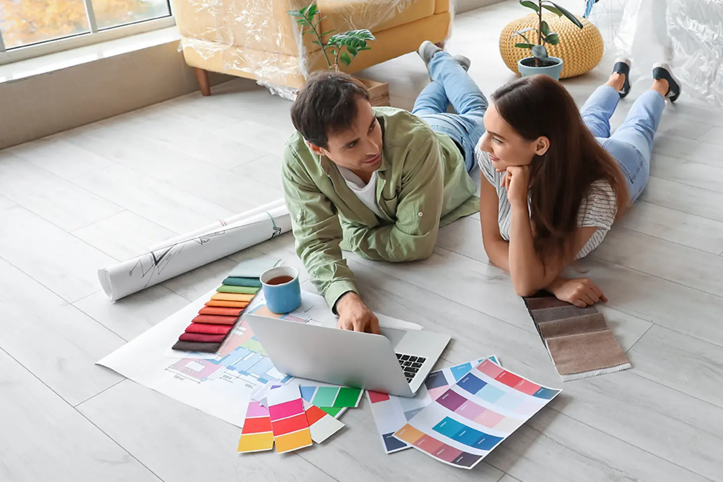 Jeune couple rénovant un appartement, choisissant en ligne les lames de parquet et le papier peint.