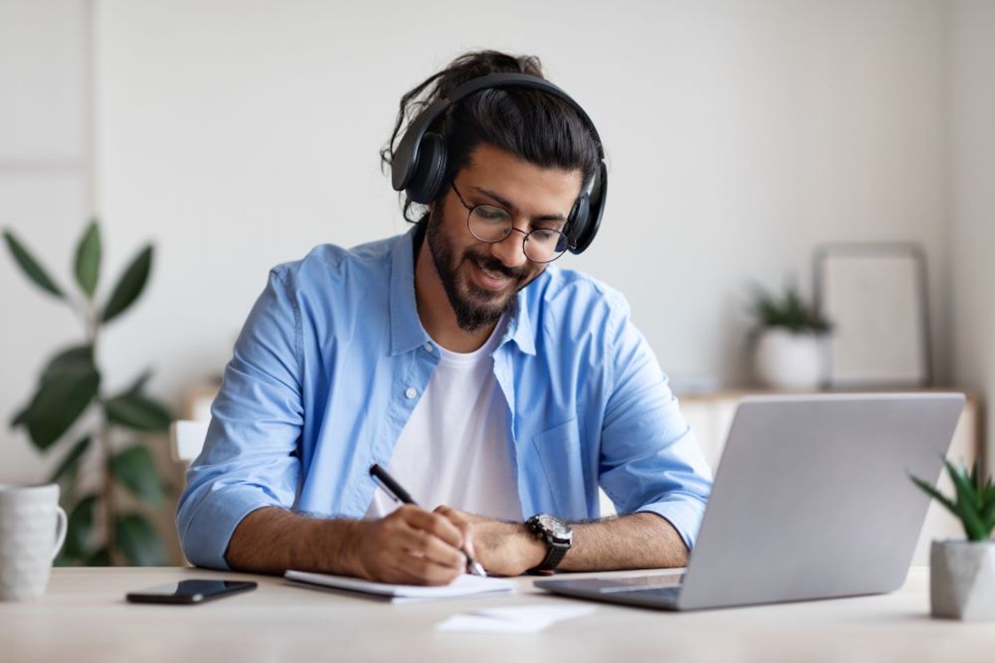 Mann studiert am Laptop mit Kopfhörern und macht Notizen.