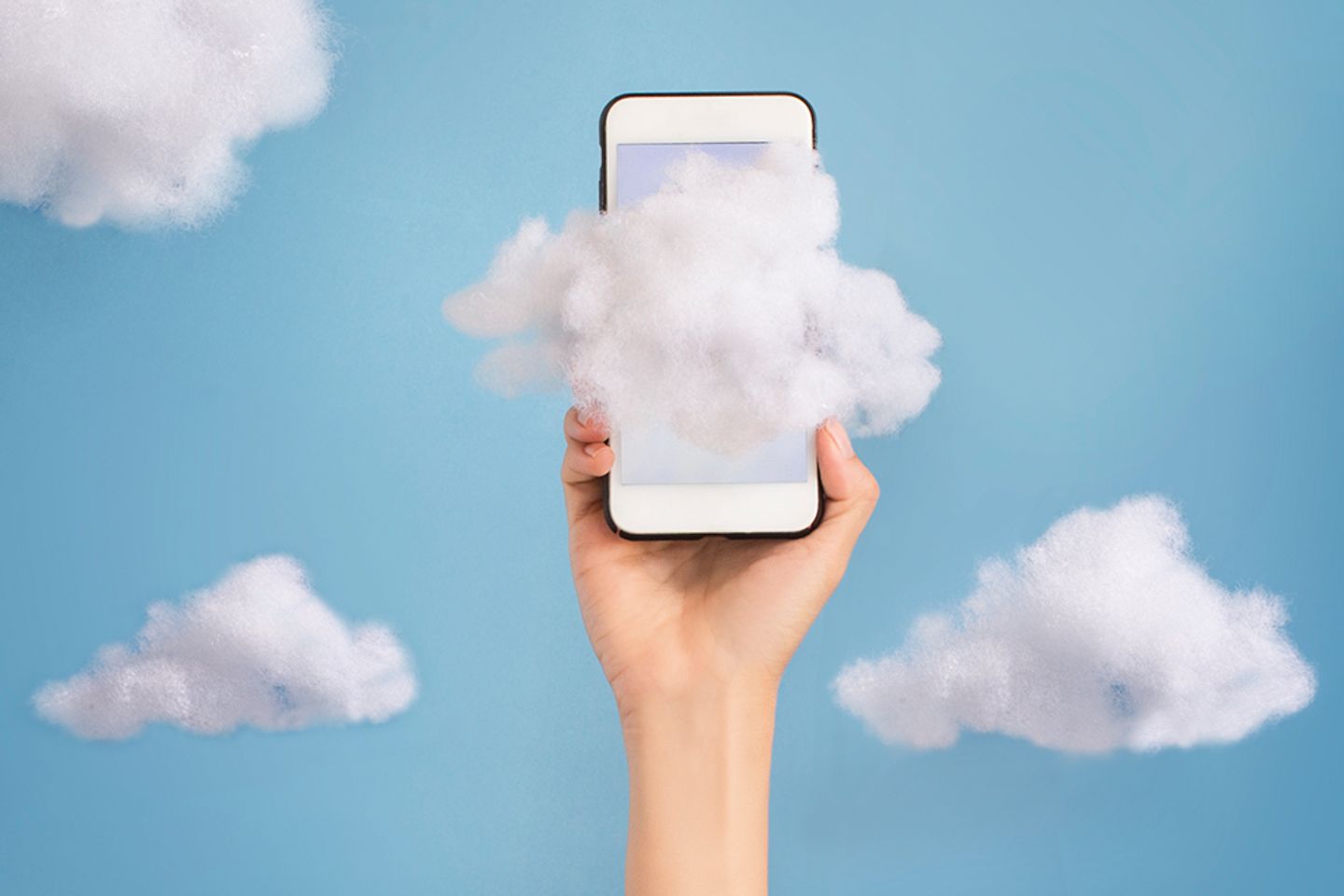 Eine Hand hält ein Handy hoch in den Himmel vor wolkigem Hintergrund
