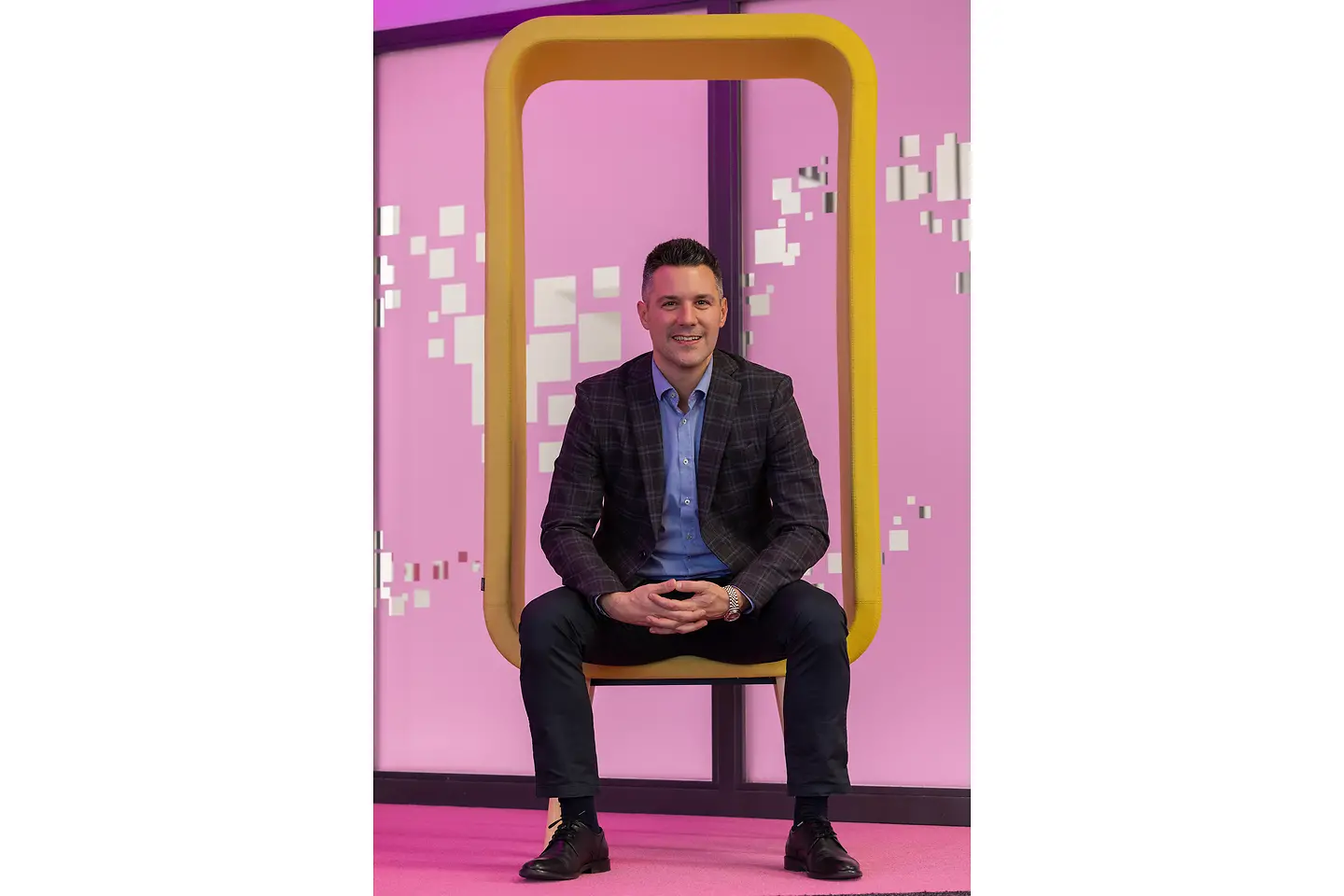 Der Sales-Profi sitzt in einem gelben Sitzelement vor dem magentafarbenen Eingang
