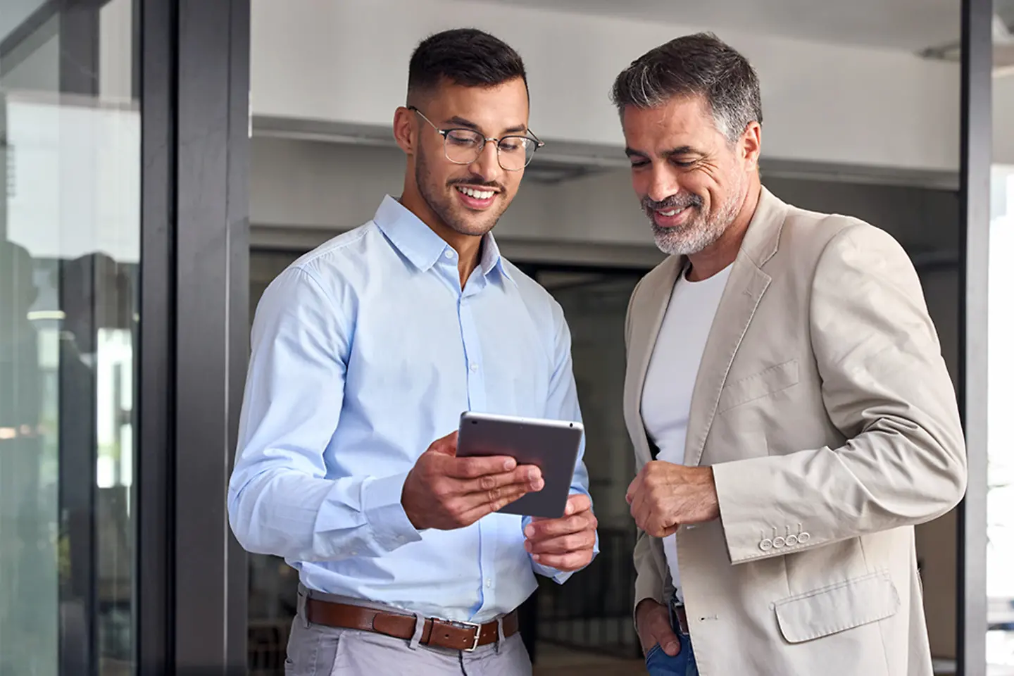Dos hombres de negocios alegres trabajando juntos en una oficina. Están de pie y utilizan una tableta digital.