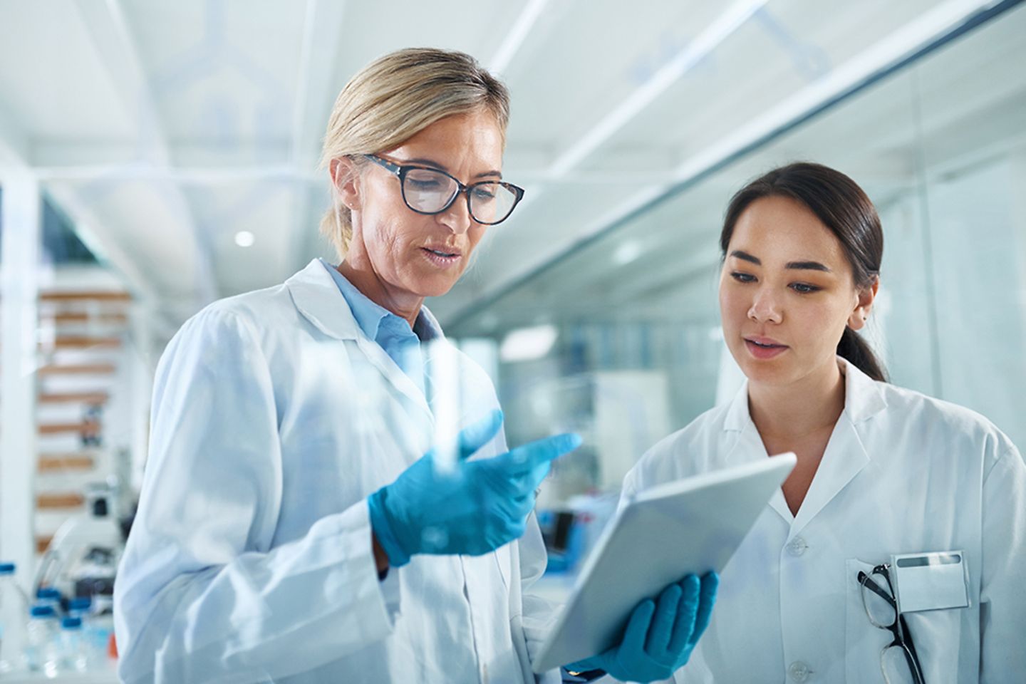 Female scientists in discussion inside a lab with a tablet.