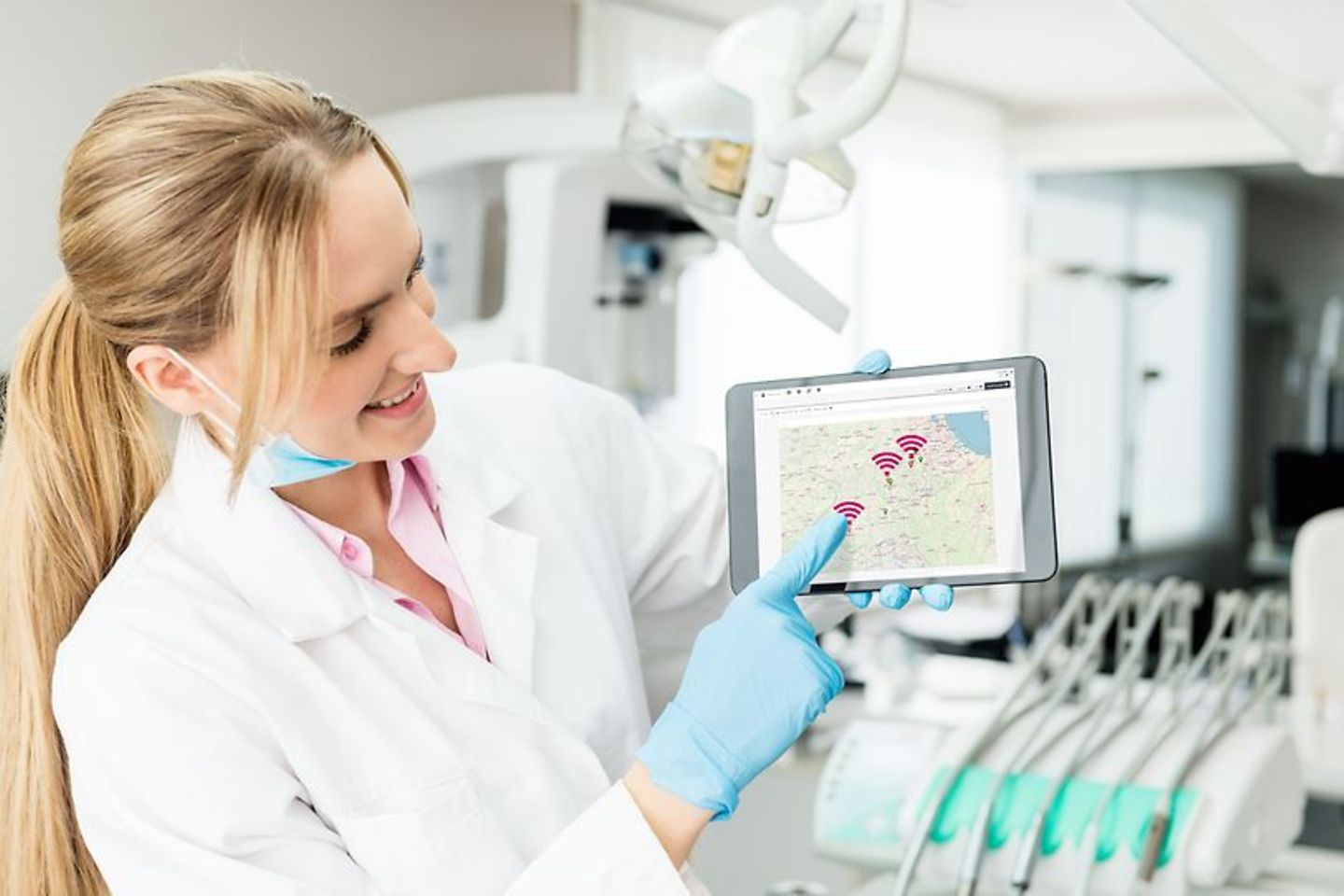 A woman in a doctor's coat is holding a tablet in her hand and points to the display.