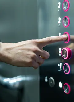 Ein magentafarbiger Knopf wird von einer Person im Aufzug gedrückt