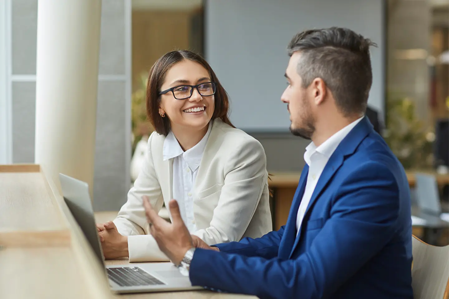 Two young smiling company employees man and woman sitting with laptop having discussion