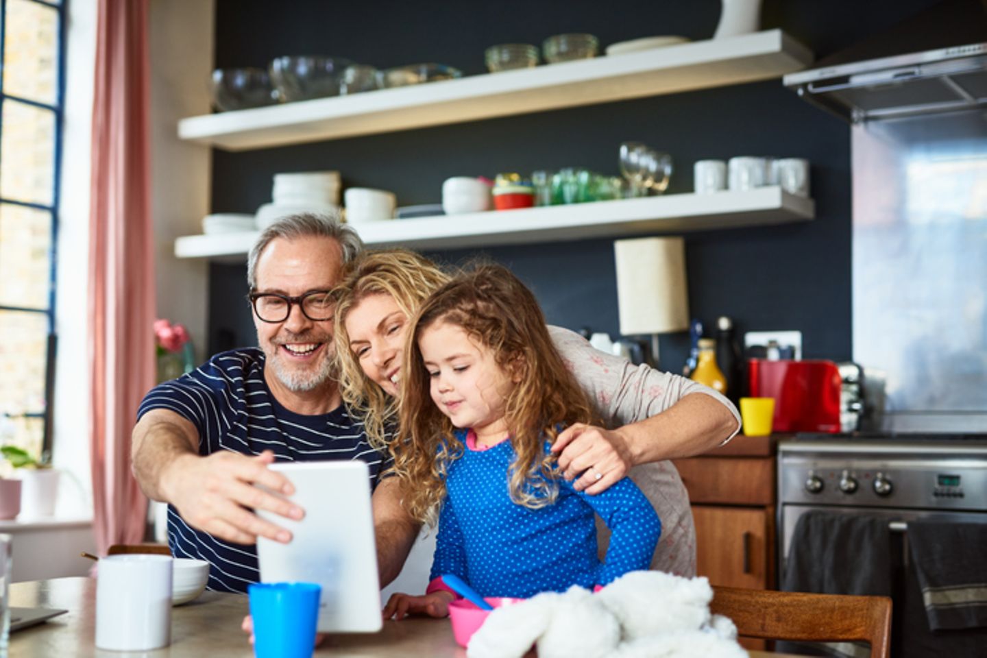 Family sitting in kitchen in front of tablet.