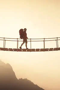 Ein Wanderer überquert eine Hängebrücke, die zwei Berggipfel verbindet