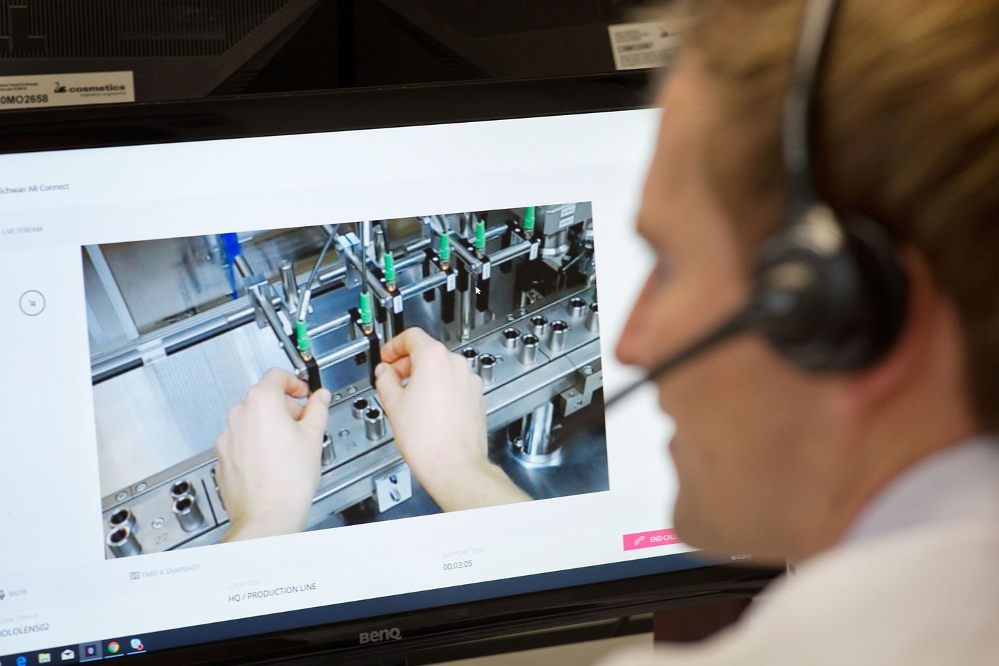 Over-the-shoulder-Aufnahme Mann mit Headset vor dem Computer. Auf dem Bildschirm sind zwei Hände zu sehen.