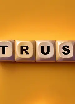 Fünf Würfel auf gelbem Grund mit den Buchstaben TRUST