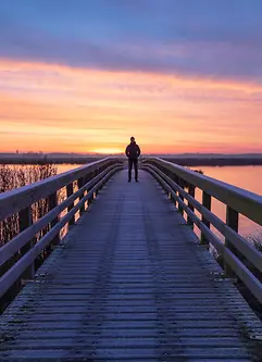 Ein Mann auf einer Holzbrücke, der die Aussicht bei einem ruhigen Sonnenaufgang genießt.