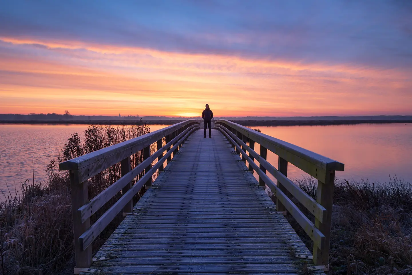 Un hombre en un puente de madera disfrutando de la vista durante un tranquilo amanecer.