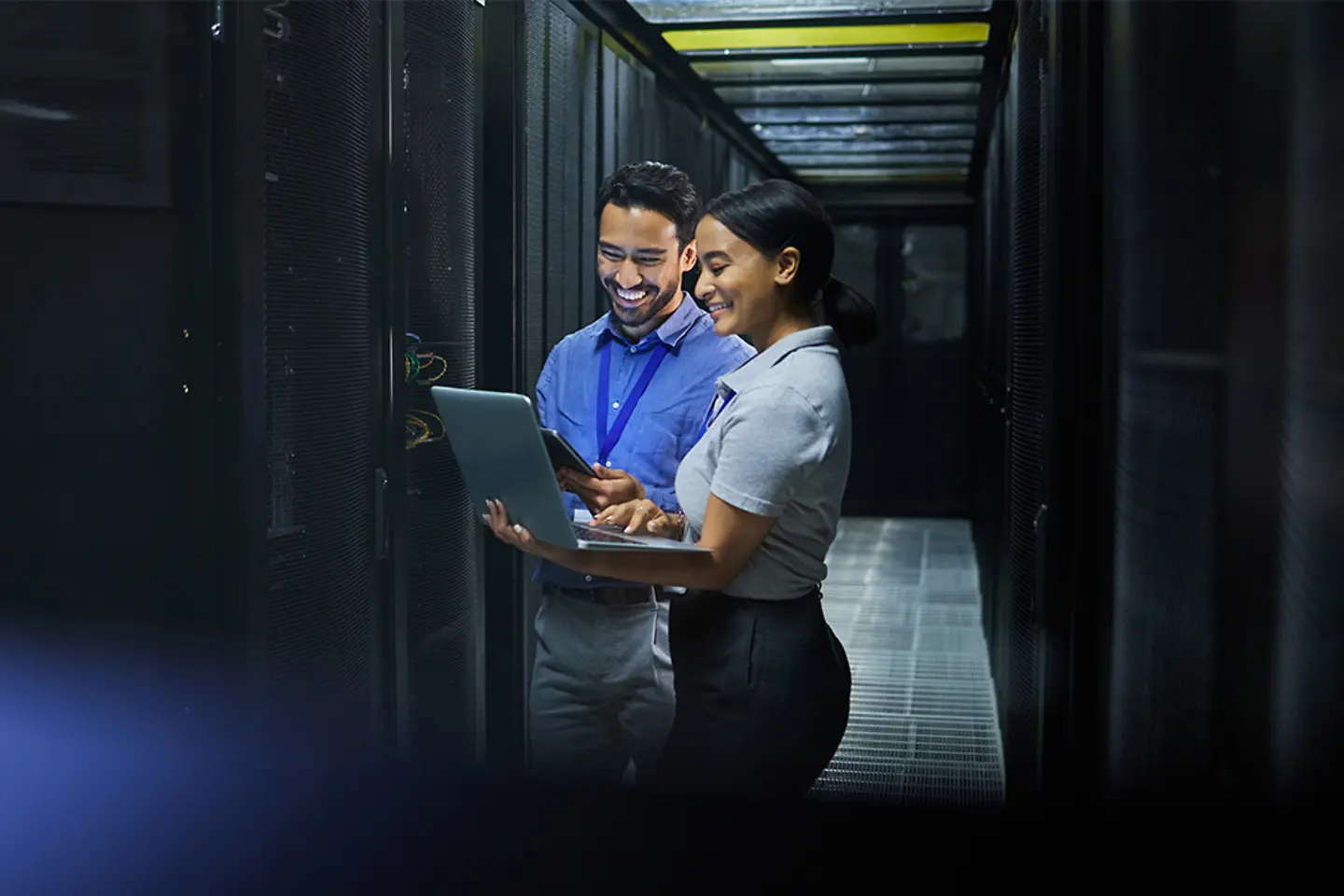 Two experts in a server room with a laptop and a tablet
