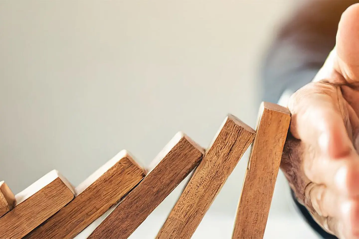 A hand halts wooden dominoes from falling over, symbolizing the prevention of a business crisis