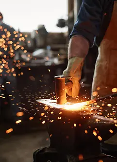 Nahaufnahme eines Schmieds in einer Schürze, der in seiner Werkstatt mit Hammer und Eisen arbeitet