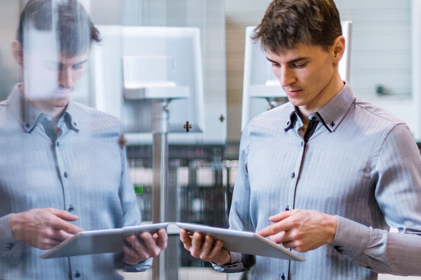 Man with tablet in front of a conveyor belt with robot arm 