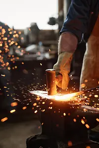 Close-up of blacksmith in apron working with hammer and iron in the workshop