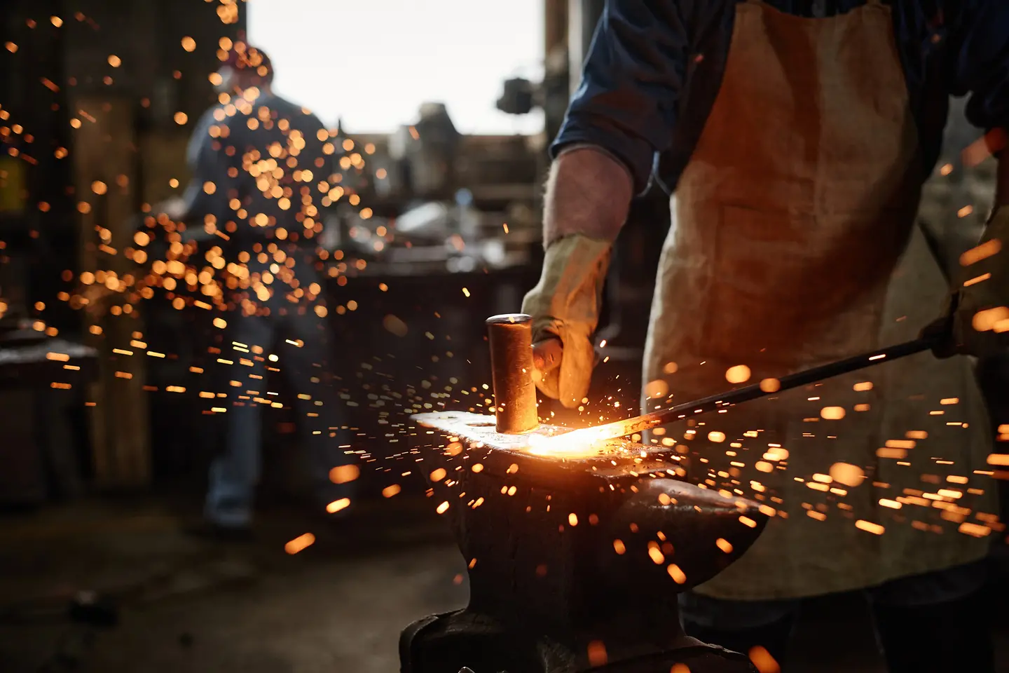 Gros plan sur un forgeron en tablier travaillant au marteau et au fer dans son atelier.