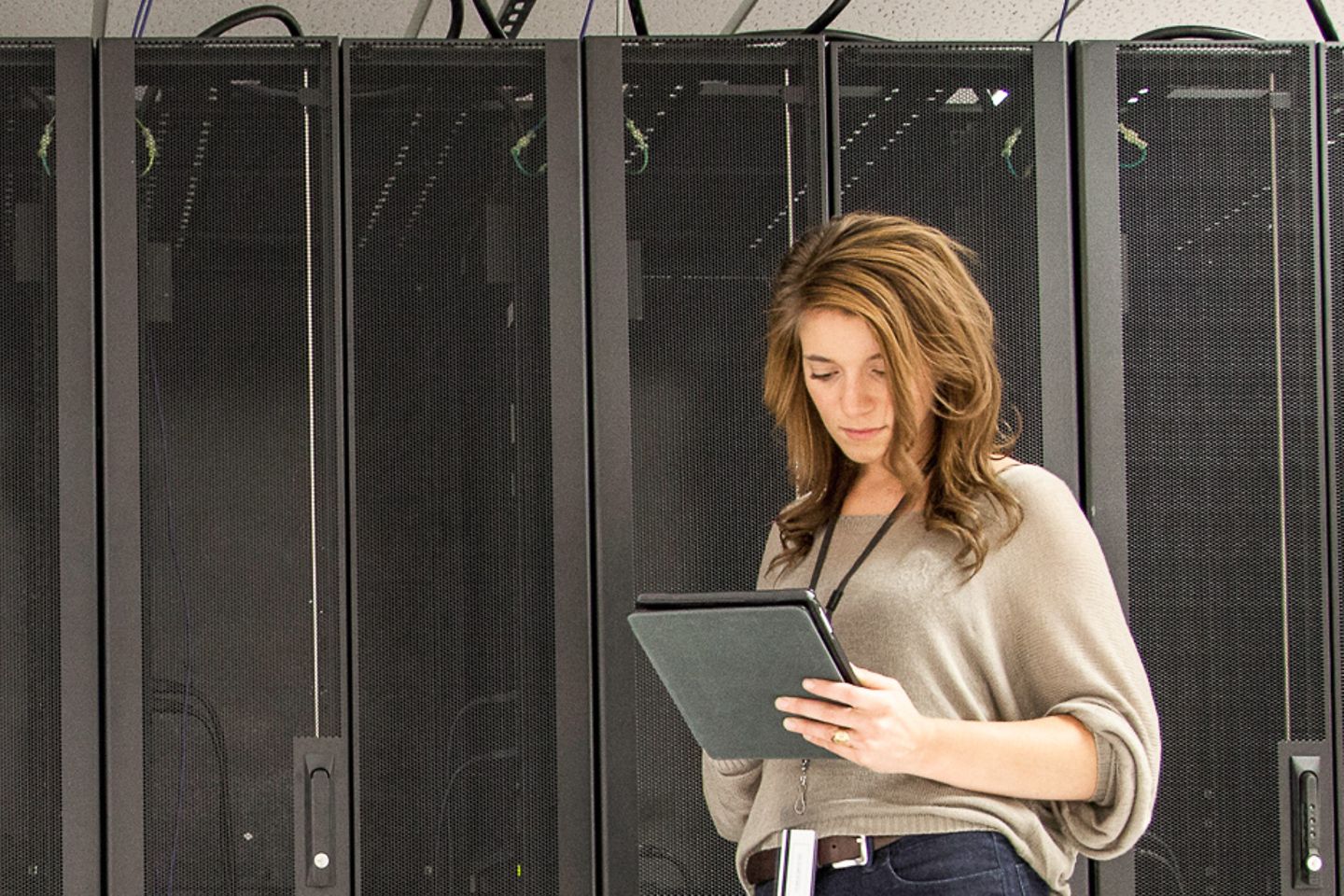 Businesswoman stands in front of servers racks and works on a tablet