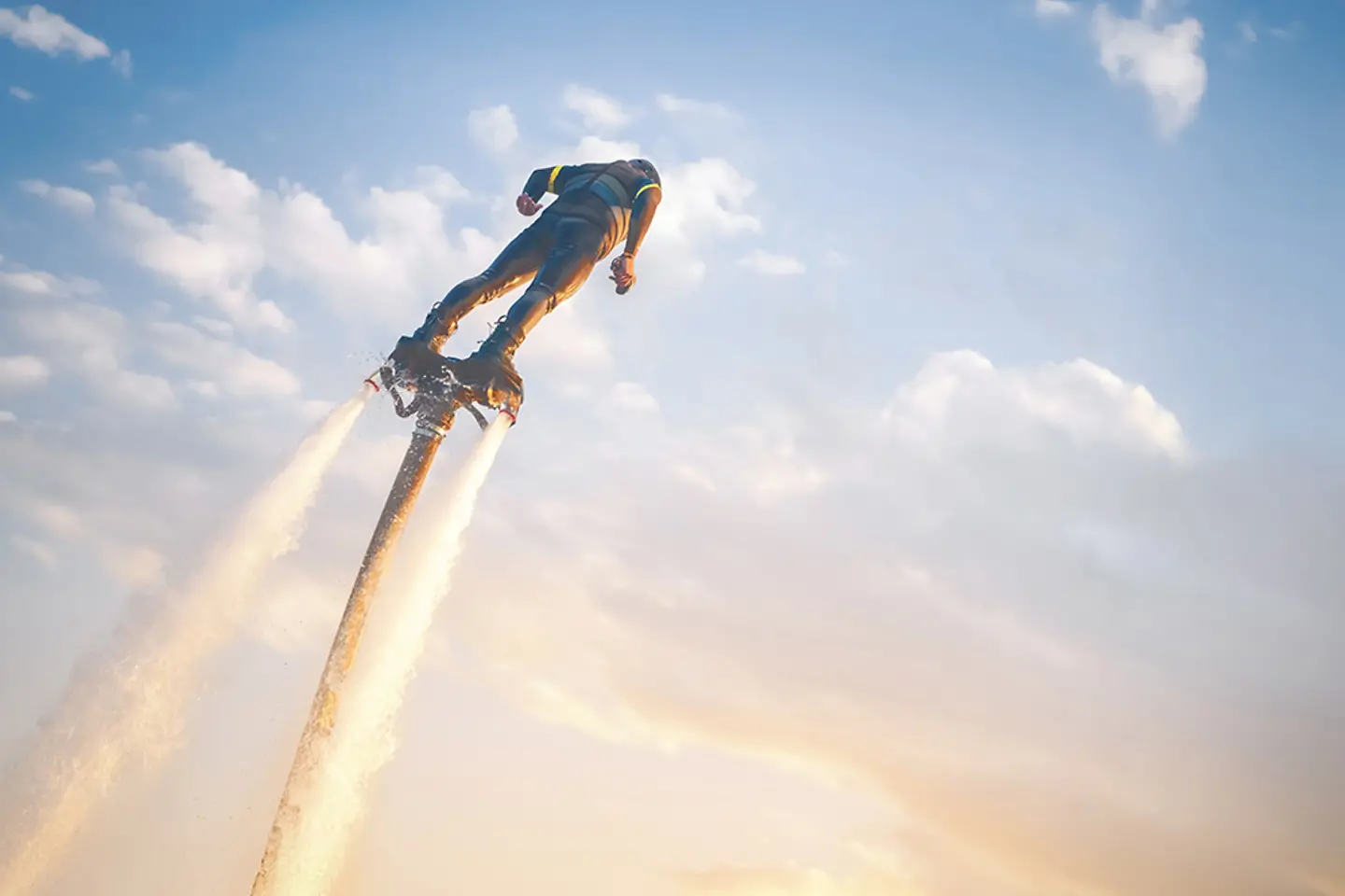 Un flyboarder flotte au-dessus de l’eau sur fond de coucher de soleil, porté par de puissants jets d’eau.