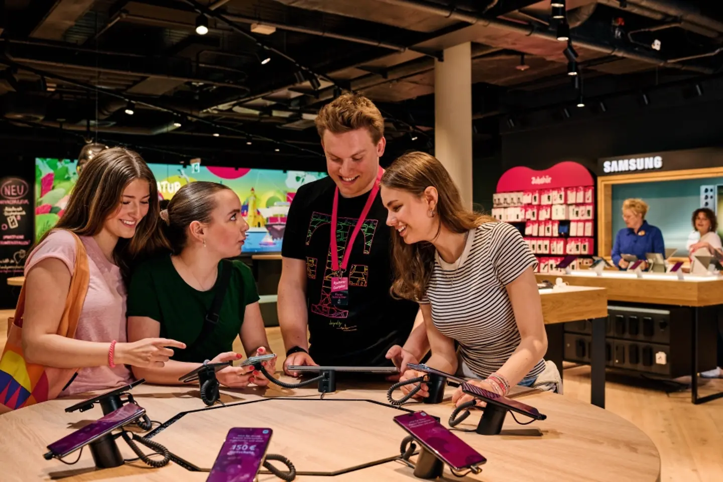 Drei Kundinnen werden von Mitarbeiter zu Mobiltelefonen in einem Flagship Store beraten