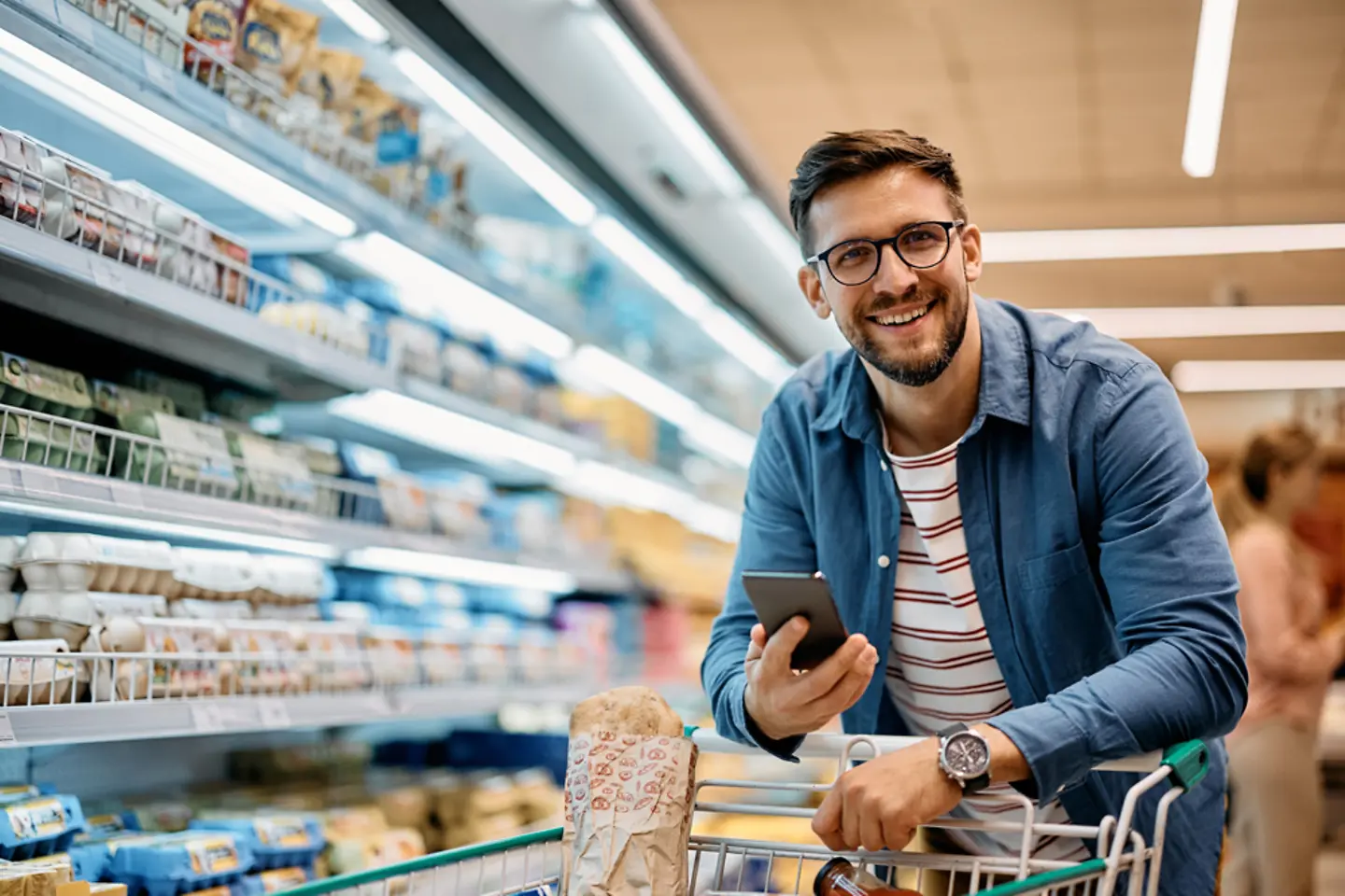 Happy man using mobile phone app while buying groceries in supermarket