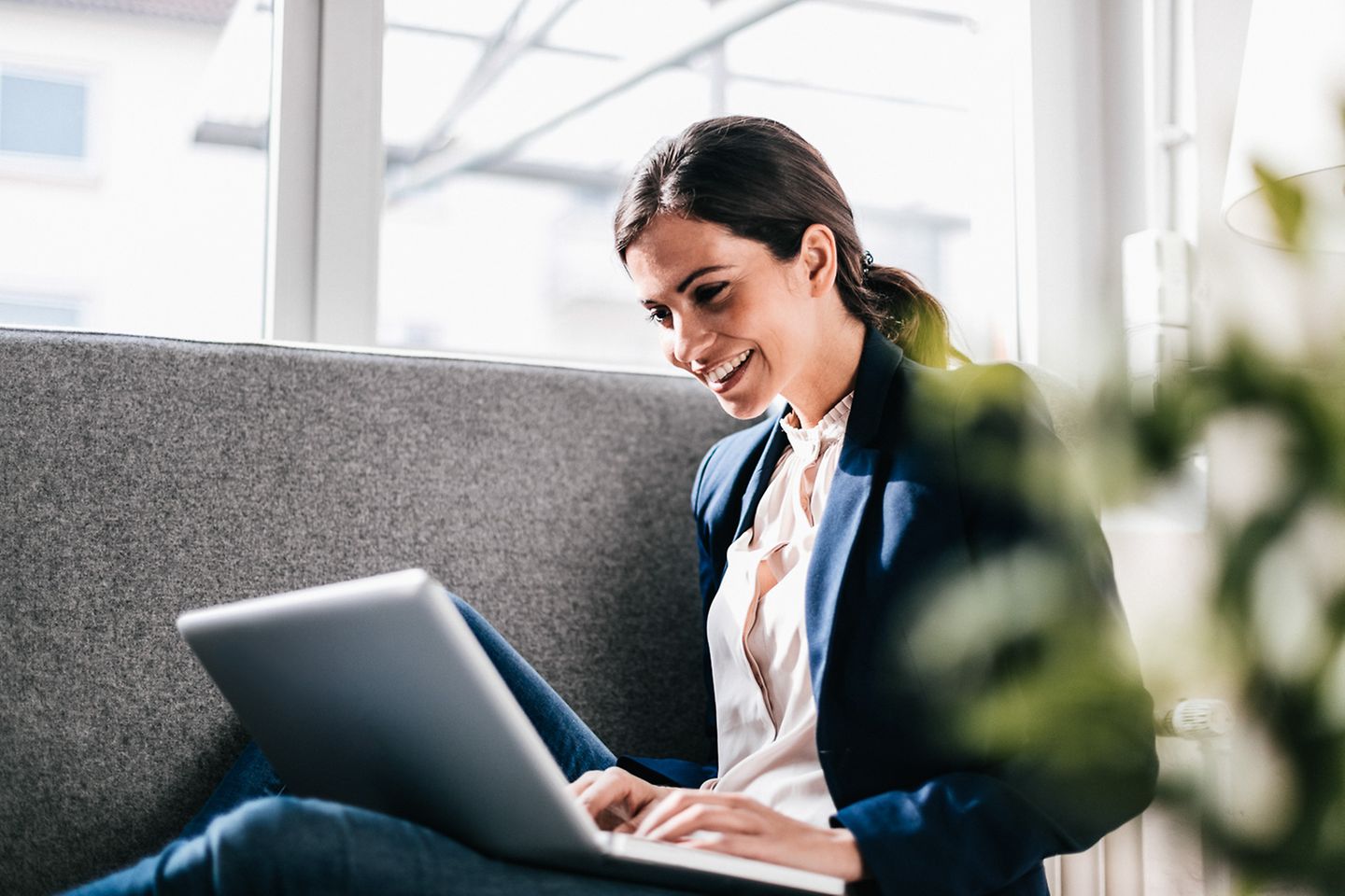 Woman is sitting with the laptop on the lap and smiling