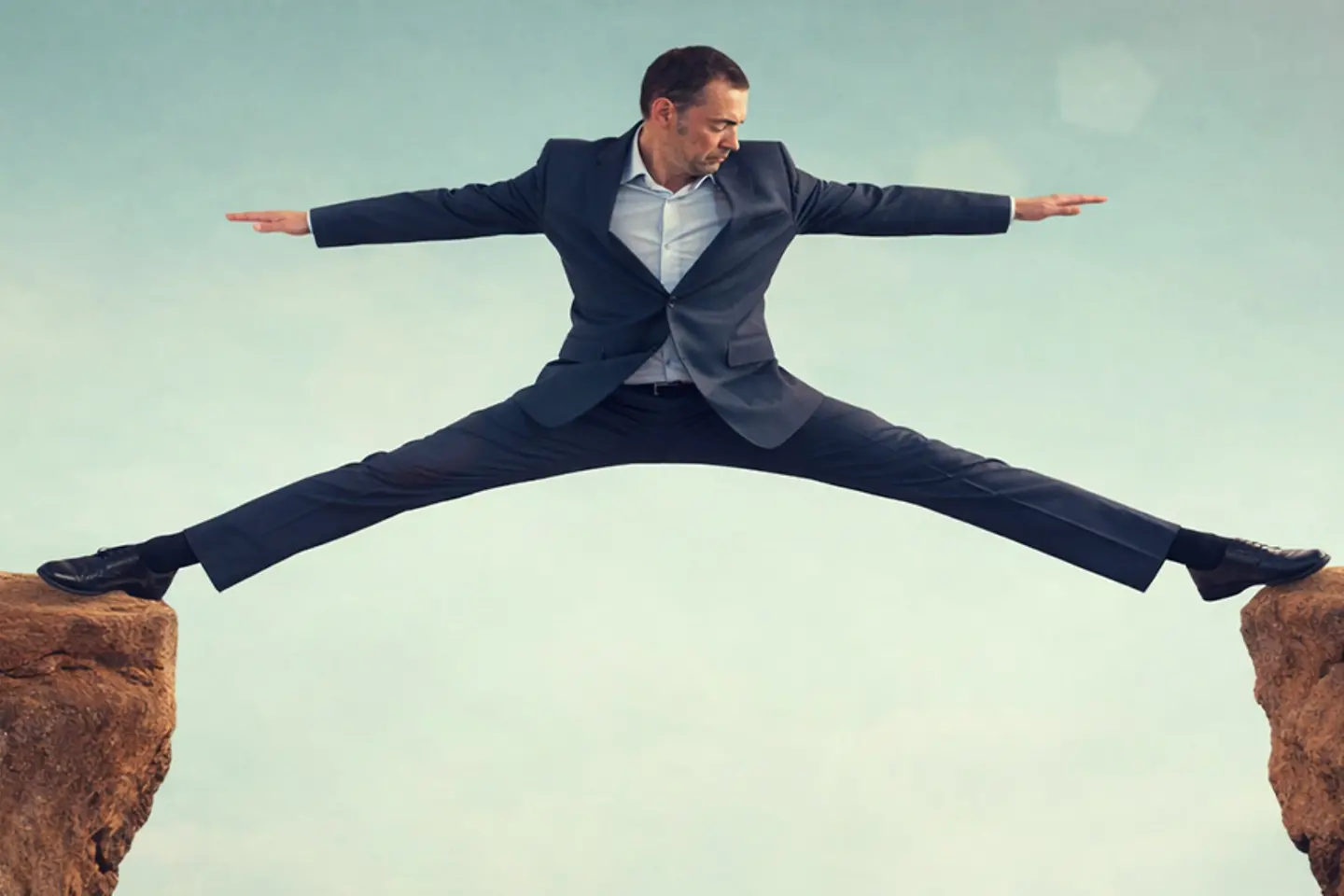 KI-generiertes Bild - Ein Geschäftsmann macht einen Spagat von einer Bergspitze zur Anderen