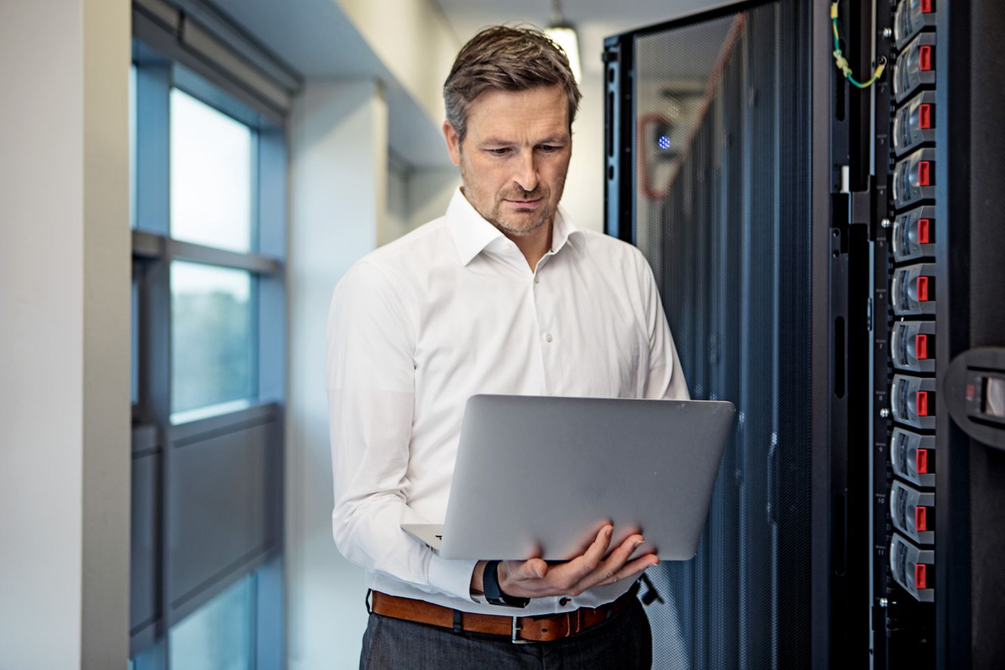 Man with laptop in hand works in front of an open server cabinet