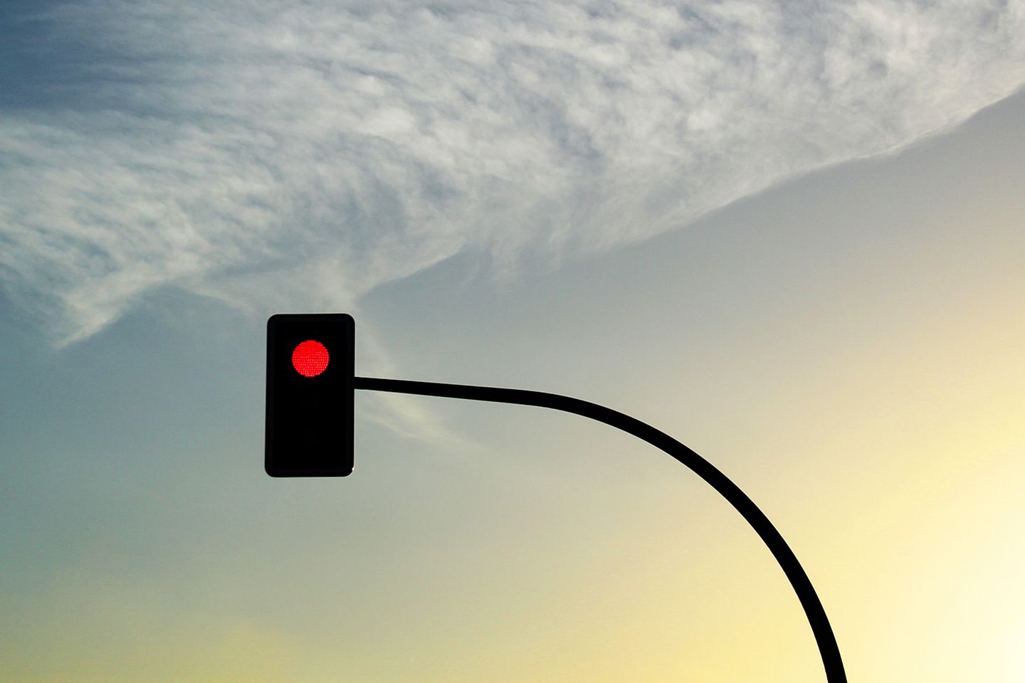 Malerische Aufnahme einer Wolkenkonstellation bei Dämmerung, davor ist eine rote Ampel zu sehen.