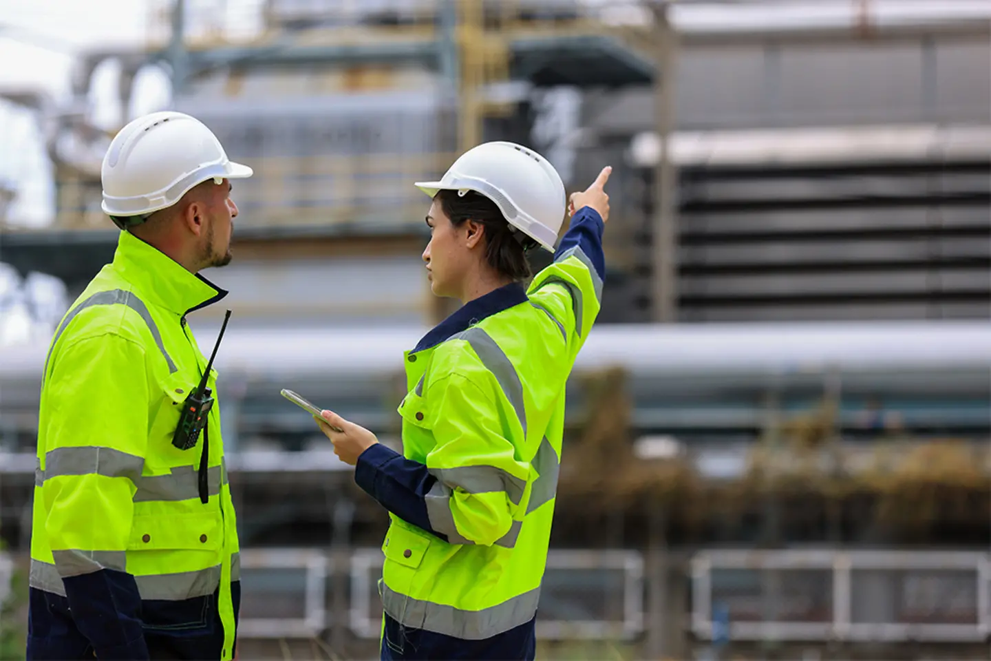 Team of engineers discussing safety protocols using digital tablet for predictive maintenance in oil and gas refinery.