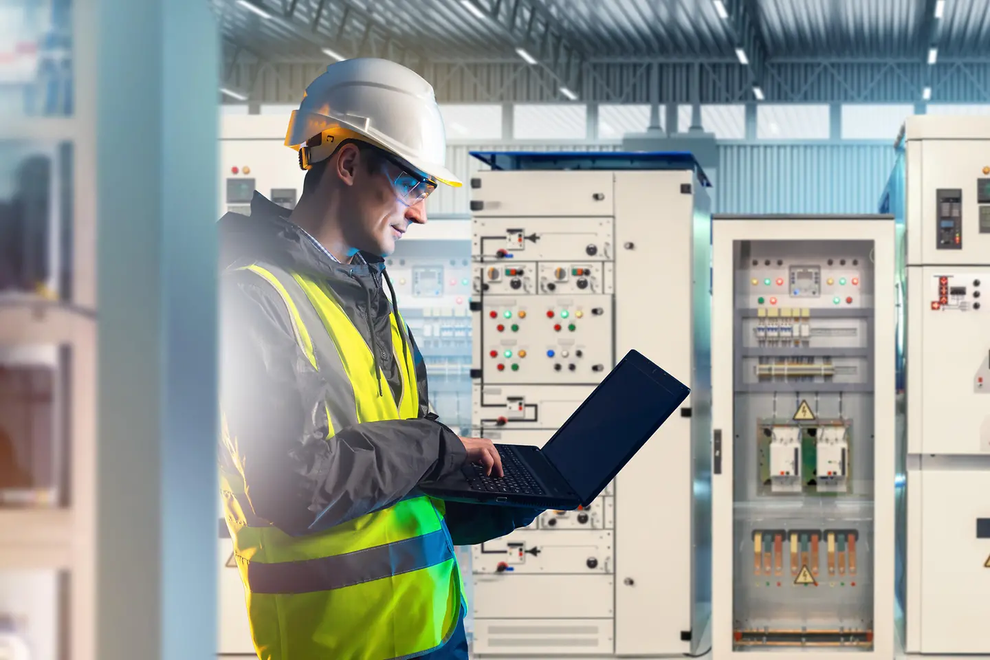 Engineer uses laptop in switchgear room, system diagnostics and industrial energy management.