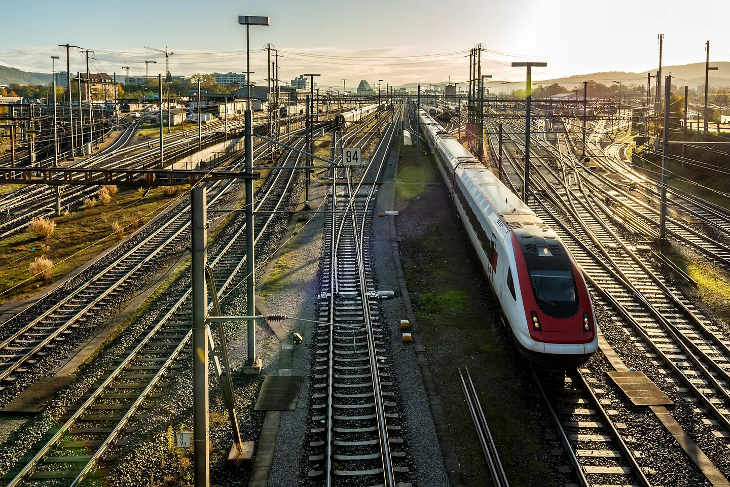 Moderner Pendlerzug an einem europäischen Bahnhof bei Sonnenaufgang mit Gleisen und Zügen