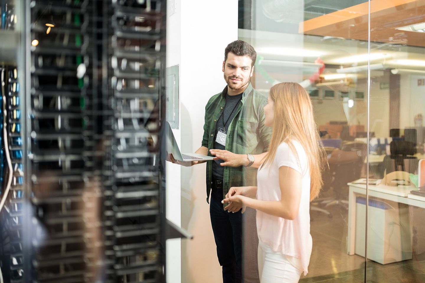 Two colleagues with laptop standing in front of a server rack talking