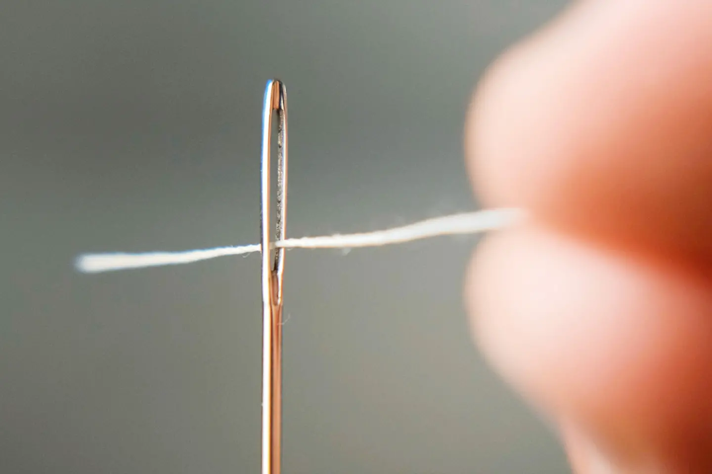 Makroaufnahme einer Hand, die einen weißen Faden durch das Nadelöhr einer Nadel führt