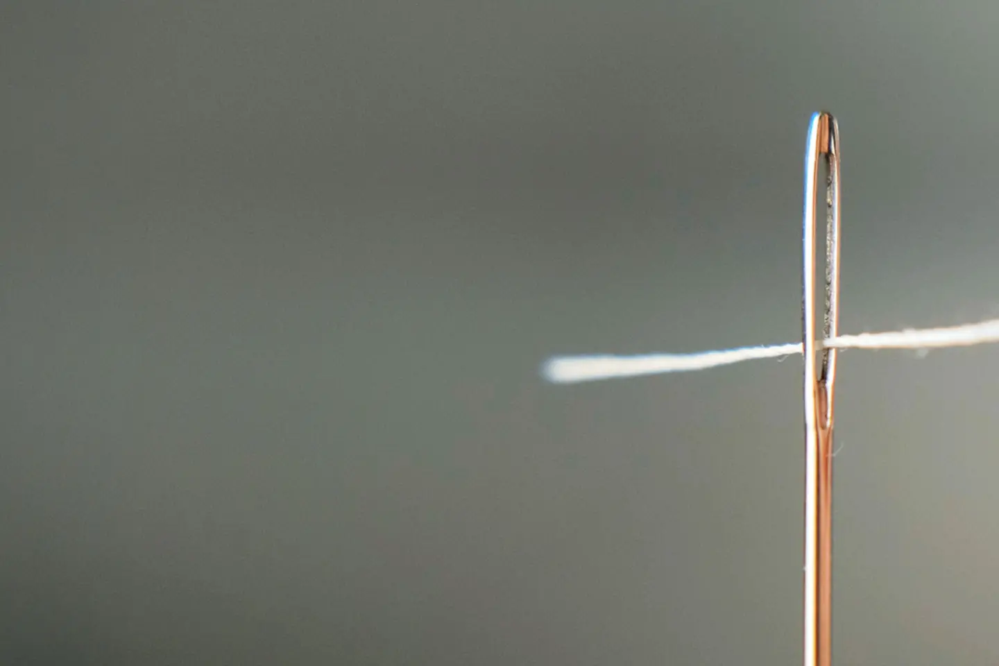 Macro shot of a hand threading a white thread through the eye of a needle