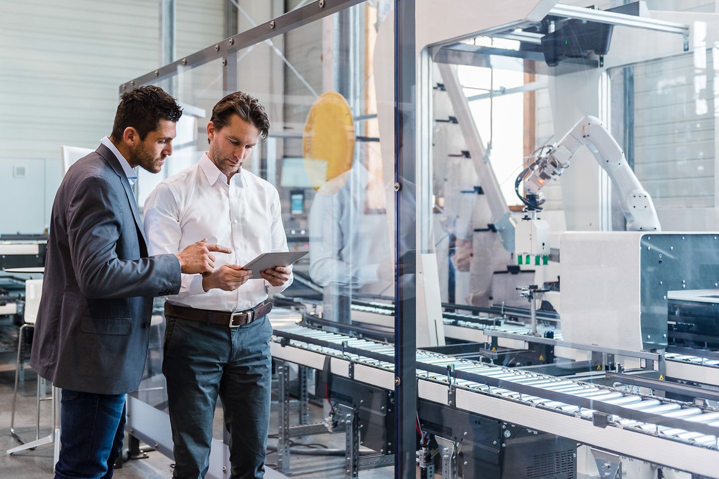 Two businessmen with tablet discuss in front of modern industrial plant