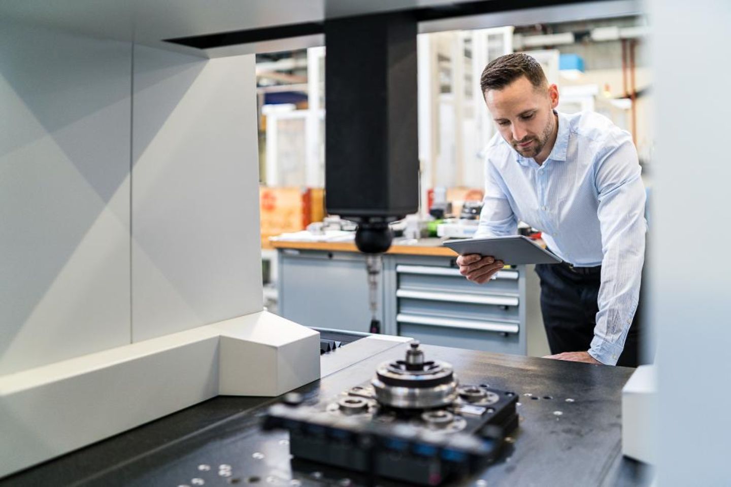  Businessman stands with tablet in hand over a machine