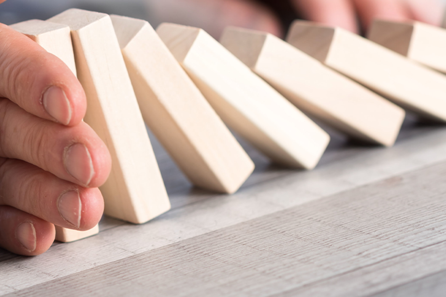 Hand stoppt Domino Steine vor dem Fallen