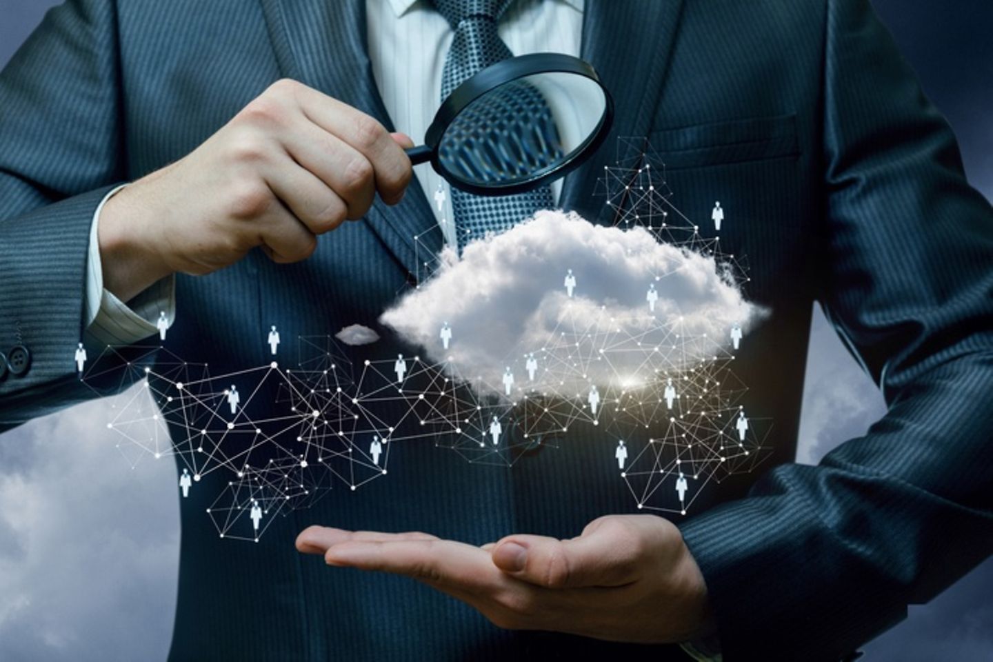 A businessman holds a magnifying glass under which there is a cloud and a graphic representation of a personnel structure.
