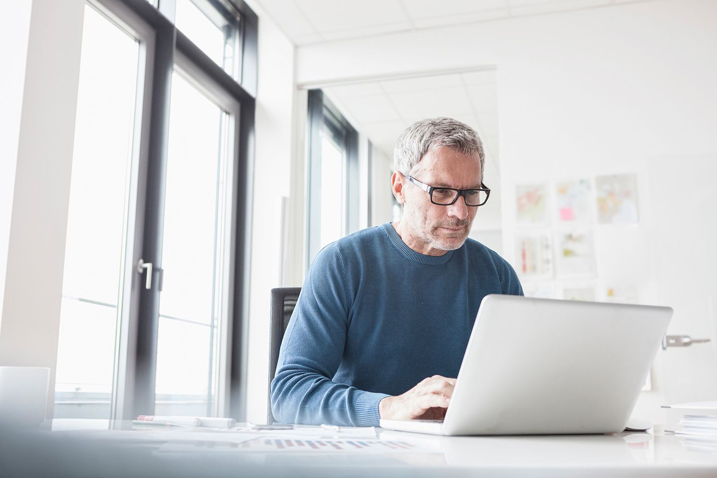 Middleaged, focused businessman sits in bright office in front of laptop