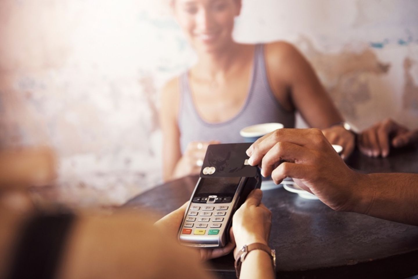 Card reader in the foreground on which a credit card is held for contactless payment.