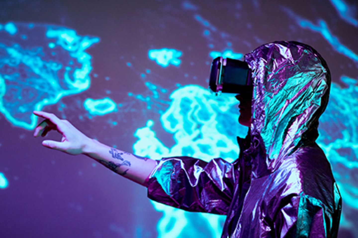 Mann in Silberanzug mit futuristischer VR-Brille zeigt auf eine leuchtende Weltkarte.