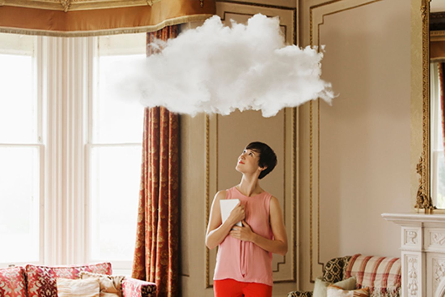 Frau steht in Wohnzimmer und schaut hoch zu einer kleinen weißen Wolke über ihrem Kopf.
