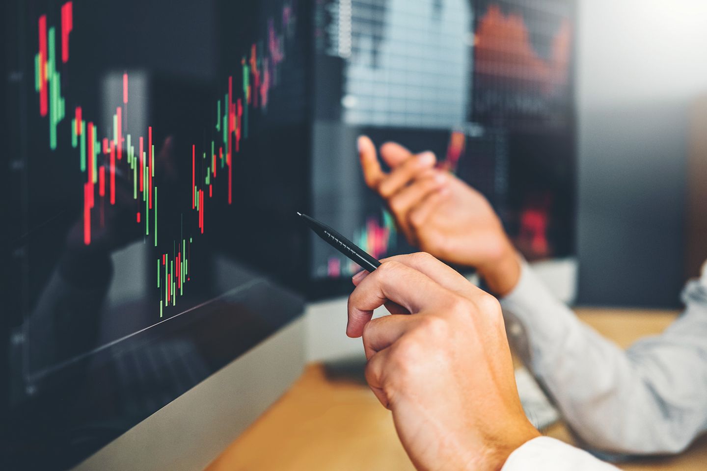 Hands gesturing in front of a computer screen showing a linear progression similar to a stock market quote.