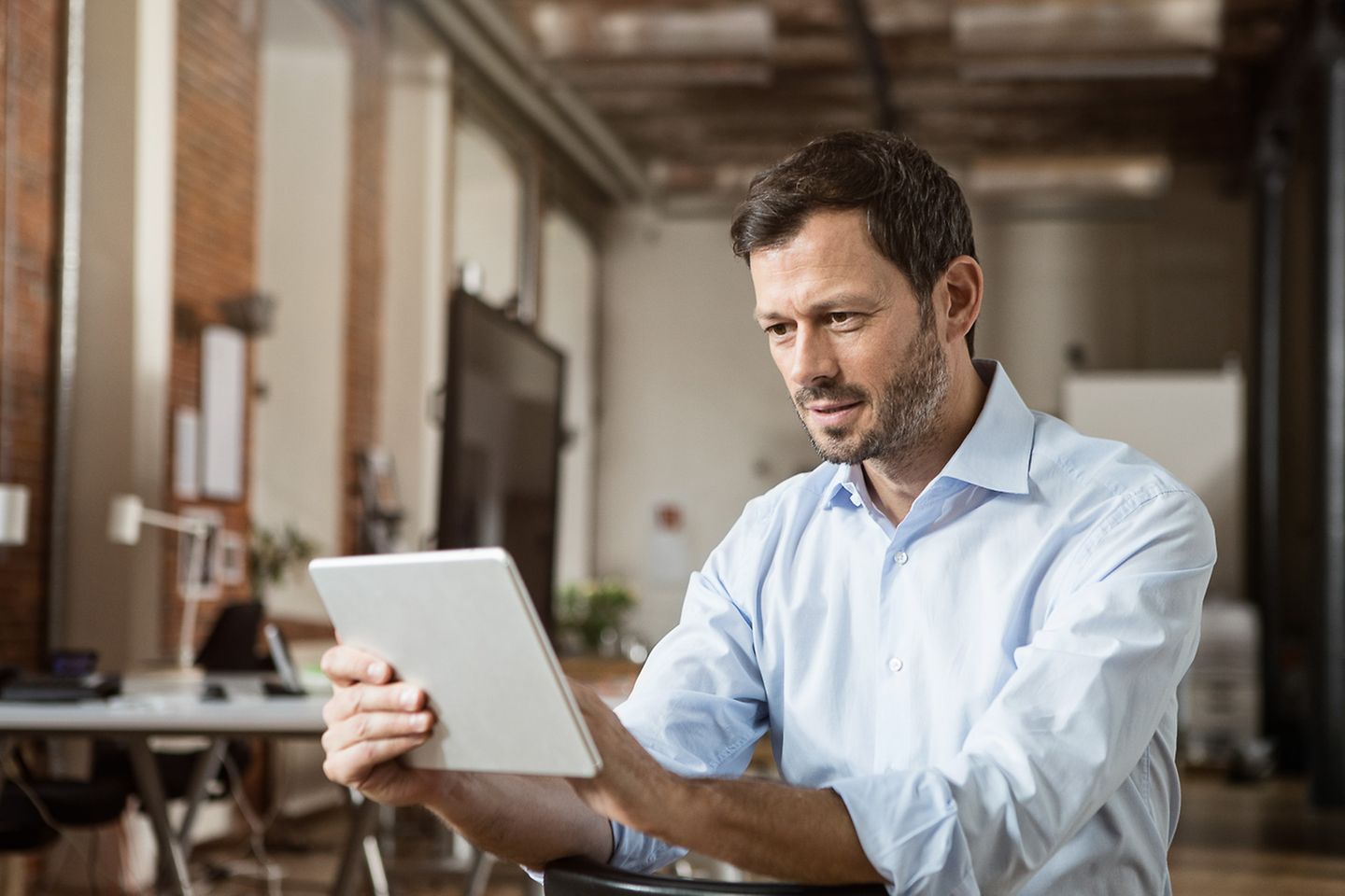 Man in an office room is reading and typing something on his tablet