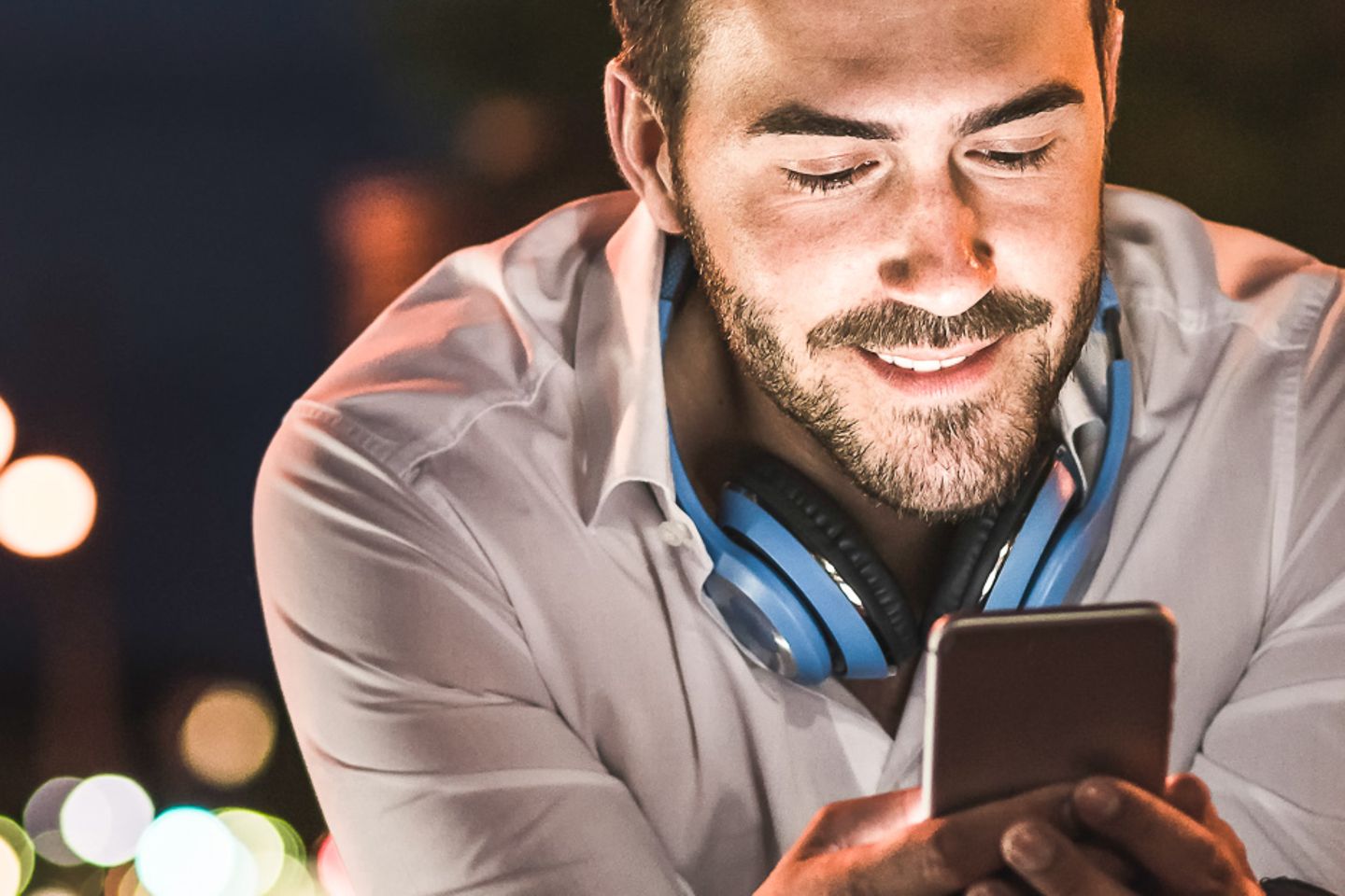  Young man in urban environment looks at illuminated smartphone display at night